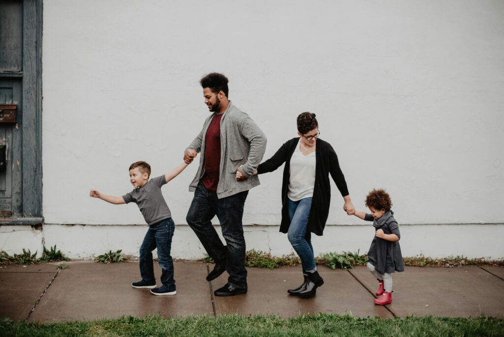 A mom and dad walking with their two young children, all holding hands